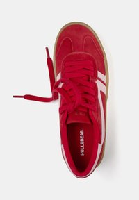 Baskets en daim rouge avec bandes blanches, bout rond, semelle en caoutchouc et lacets rouges assortis. Marque visible sur la semelle intérieure. Vue de dessus.