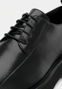 Scarpa nera in pelle con una superficie liscia e lucida. Presenta una punta arrotondata, un design con stringhe e una suola bassa e robusta.