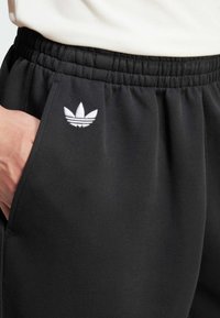 Sorte sweatpants med elastisk talje og sidelomme. Har et hvidt broderet logo på venstre lår. Glat tekstur.