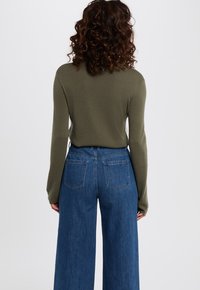 Olijfgroen langemouwen top met ronde hals, gecombineerd met hoge taille wijde blauwe spijkerbroek met twee achterzakken.
