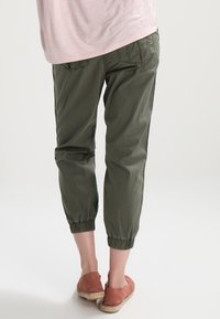 Olivgrön bomullsbyxor i cropped stil med elastiska muddarna, med bakfickor, i kombination med ljusbruna espadrillos.