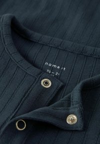 Ciemnoniebieska, prążkowana tkanina z okrągłym dekoltem. Zawiera srebrne napy przy kołnierzu. Metka wskazuje rozmiar 1½ - 2 lata.