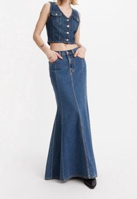 Denimový crop top s V-výstřihem a čtyřmi knoflíky, spojený s dlouhou, rozšířenou denimovou sukní; oboje v středně modré barvě s viditelným švem.