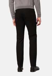 Czarne dżinsy o prostym kroju, z klasycznym stanem, delikatnymi tylnymi kieszeniami i gładką fakturą. Noszone z szarym swetrem.