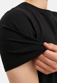 Schwarzes Baumwoll-T-Shirt mit kurzen Ärmeln, Nahaufnahme, die die weiche Textur und die sauberen Nähdetails am Saum und an den Ärmeln zeigt.