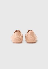Lichtroze instapschoenen met een gestructureerd ontwerp, featuring golvende lijnen, een afgeronde vorm en een gladde rubberen materiaal. Geen zichtbare merkdetails.
