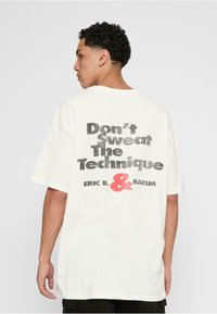 Hvid bomulds T-shirt med korte ærmer, prydet med en stor sort og rød grafisk tekst på ryggen: "Don't Sweat The Technique, ERIC B. & RAKIM."