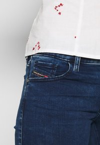 Mörkblå denimjeans med en klassisk femfickdesign, visar en distinkt etikett i framfickan och en slät textur.