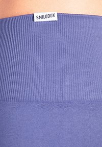 Vita a costine color navy con una transizione fluida a un tessuto solido sottostante; presenta un piccolo tag bianco con l'etichetta "SMILODOX".