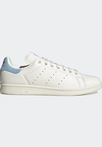 Vita lädersneaker med ljusblå accenter, perforerade sidodetaljer, platta snören och en texturerad gummisula. Adidas-logotyp på hälen.