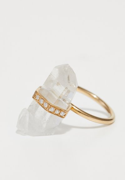 Clear quartz ring featuring a gold band with diamond accents wrapped around the crystal, showcasing a natural, angular shape.