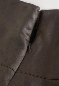 Ingrandimento di una giacca di pelle marrone scuro parzialmente zipata che mostra in dettaglio la texture e le cuciture.
