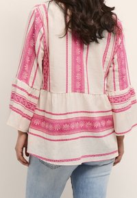 Lehounká béžová blůza s růžovými vertikálními pruhy, květinovými vzory a rozšířenými rukávy. Navržena s peplum pasem. Casual střih.
