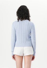 Light blue cable-knit sweater with a ribbed collar and hem, long sleeves, and a textured pattern; worn over white striped shorts.
