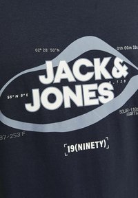 Navyblauwe katoenen t-shirt met witte en lichtgrijze tekst. Het ontwerp bevat geografische coördinaten en de merknaam "JACK & JONES."