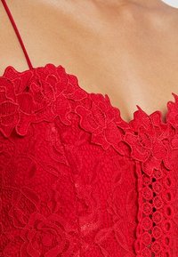 Bodice en dentelle rouge avec motif floral et détails texturés. Présente des bretelles délicates et un décolleté festonné. Accents décoratifs subtils.