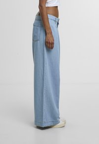 Light blue wide-leg jeans made of denim. Features include a high waist, side pockets, and a clean hem. Paired with white sneakers.