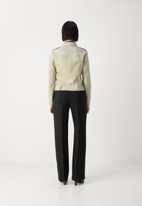 Jachetă din piele crem cu epauleți pe umeri și croială ajustată, asortată cu pantaloni negri cu picior larg și tocuri negre elegante.