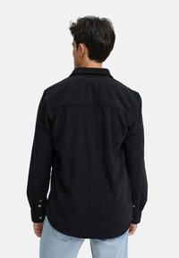 Camicia in corduroy nera con colletto button-down, maniche lunghe e motivo a coste testurizzate, vista dal retro.