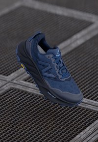 Botte de sport bleu marine avec tige en mesh, détails texturés et semelle extérieure en caoutchouc. Présente un logo "N" en évidence et des accents Vibram.