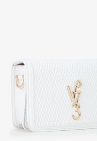 Witte gequiltte leren handtas met een goudkleurig logo en hardware, met een rechthoekige vorm en contrasterende rode binnenvoering.