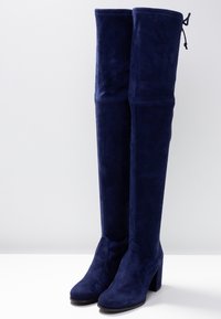 Marineblaues Wildleder-Überknie-Stiefel mit Blockabsatz. Glatte Oberfläche mit umgeschlagenem Schaft und verstellbaren Bändern oben.