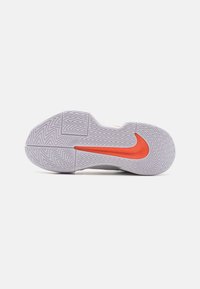 Sko med en struktureret gummisål, der har et fremtrædende rødt Nike-logo og et zigzag-mønster, primært hvidt med orange detaljer.