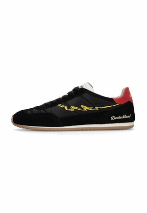 Czarny sneaker z żółtym detalem w zygzag, czerwoną zakładką na pięcie, białą podeszwą oraz wyszywanym po kremowemu napisem "Deutschland" na boku.
