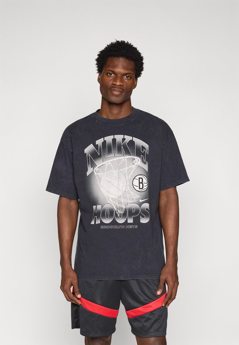 Tmavě šedé bavlněné tričko s grafikou basketbalové sítě, textem "NIKE HOOPS" a detailem "BROOKLYN NETS". V kombinaci s černými šortkami s červenými pruhy.