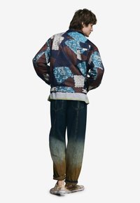 Kurtka w wielokolorową łatę z wzorami w odcieniach niebieskiego, brązowego i kremowego, zestawiona z niebieskimi dżinsami z efektem ombre. Złote trampki.