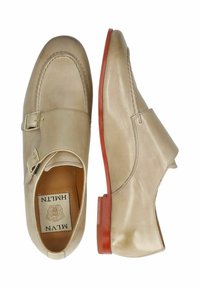 Scarpe in pelle beige con punta arrotondata, dettagli a doppia fibbia e suola rossa. Presentano una texture liscia e una cucitura elegante.