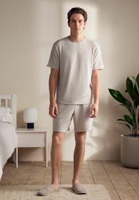 Beige ribbed short-sleeve top and matching shorts, both made from textured fabric. Light slippers complete the casual loungewear look.