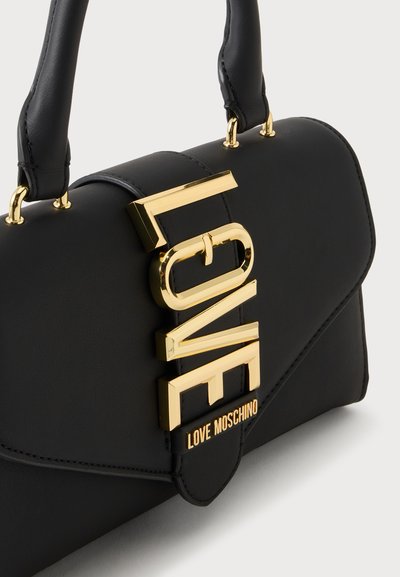 Крупен план на черна чанта Love Moschino с дръжки в златист тон и големи златни букви на предния капак.