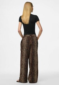 Pantalons larges à motifs léopard avec une palette de couleurs beige et marron, fabriqués en tissu doux ; associés à un t-shirt noir ajusté.