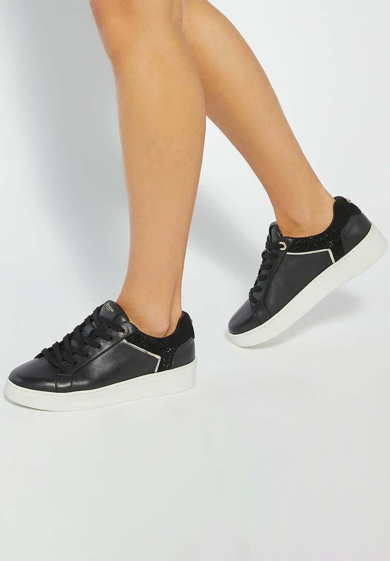 Black leather sneakers featuring a white sole, textured black accent on the heel, and a sleek design with contrasting stitching.