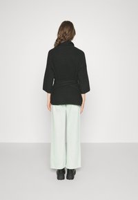 Cardigan negro texturizado con mangas anchas y cinturón anudado, combinado con pantalones de pierna ancha en un suave color menta y botas negras gruesas.
