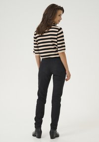 Haut rayé noir et beige avec des manches courtes, associé à un jean skinny noir. Modèle portant des bottes noires à la cheville, vu de dos.