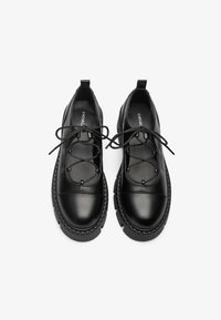 Chaussures noires en cuir avec un bout rond, un laçage, une languette rembourrée et une semelle en caoutchouc épaisse avec un bord texturé.