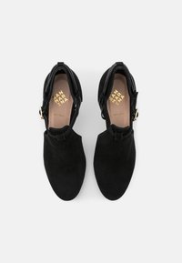 Mustat mokkanahkaiset nilkkurit, joissa on kärjellinen muoto, koristeltu solkikuvioilla ja teksturoidulla vyöllä yläosassa. Nahkavuori.