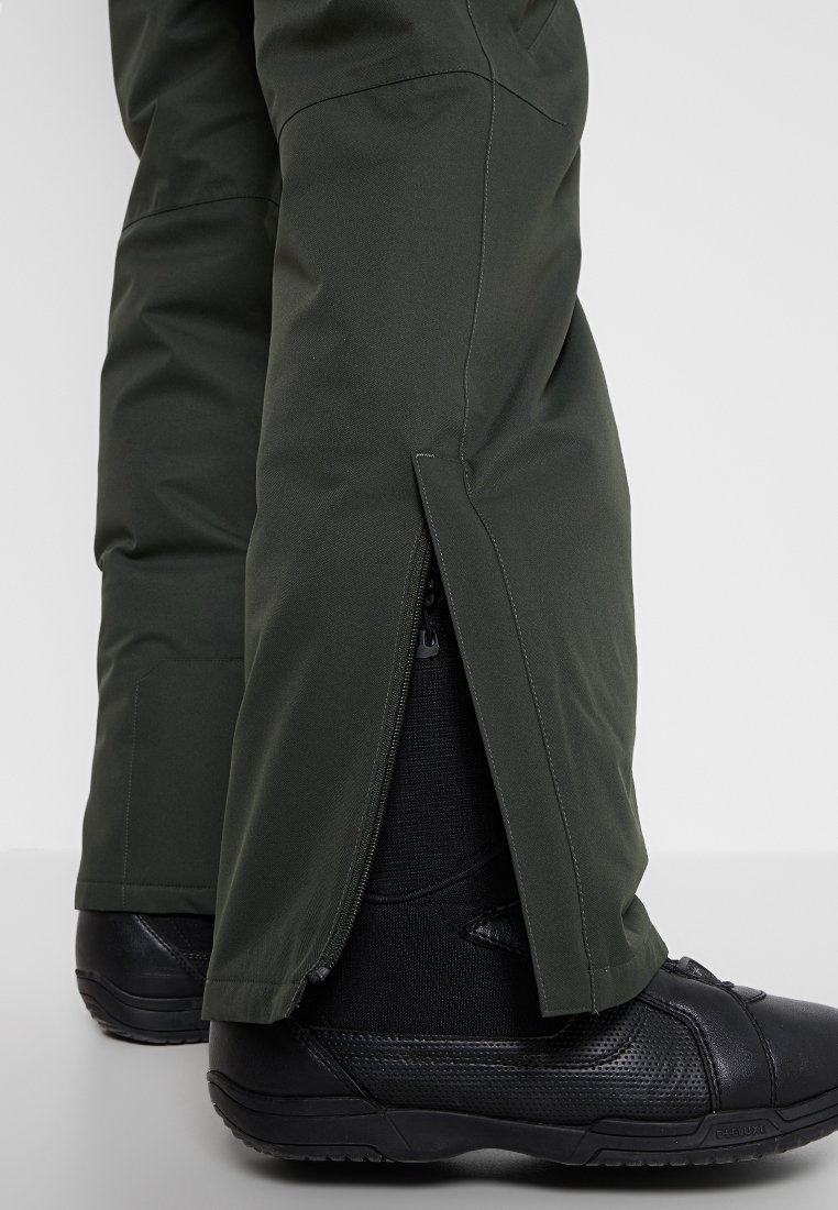 Grüne Skihosen mit Reißverschlussöffnungen an den Knöcheln, die schwarze Schneestiefel darunter zeigen. Das Material wirkt strapazierfähig mit einer strukturierten Oberfläche.