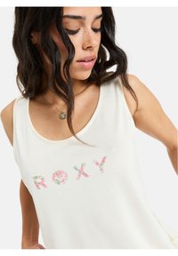 Licht crèmekleurig tanktop met een ronde halslijn, met de tekst "ROXY" in bloemenprint. Zachte stof met een comfortabele fit en zonder mouwen.