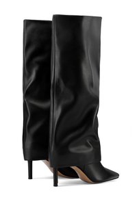 Botas altas negras de tacón delgado hechas de cuero suave, con un diseño holgado, punta afilada y tacón de estilete delgado.