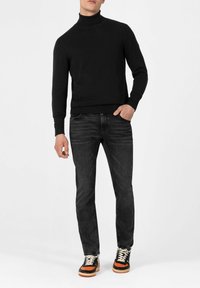 Schwarzer Rollkragenpullover, eng anliegende graue Jeans und schwarze Sneakers mit orangefarbigen und cremfarbenen Akzenten. Weiche Textur, lässiges Design.