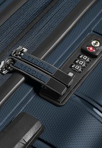 Valise bleue texturée avec double fermeture éclair métallique étiquetée Redolz, verrouillée avec un cadenas TSA noir à combinaison comportant trois molettes et une fente pour clé.