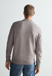Sweter crewneck w kolorze taupe, wykonany z miękkiej dzianiny z ribbowanymi mankietami i dołem. Noszony na niebieskich dżinsach, widok z tyłu.