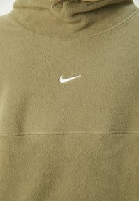 Felpa in pile verde oliva con collo alto, caratterizzata da un piccolo logo Nike bianco sul petto e una superficie in tessuto testurizzato.