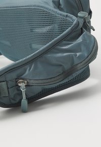 Zaino leggero blu con tasca laterale in rete, texture del tessuto liscia, chiusura con zip e tracolla regolabile con tirante in gomma morbida.