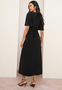 Rochie maxi neagră cu mâneci scurte, viu colorate și detaliu cu fundă în talie. Material neted cu un design fluid. Modelul poartă sandale cu toc înalt și curea.