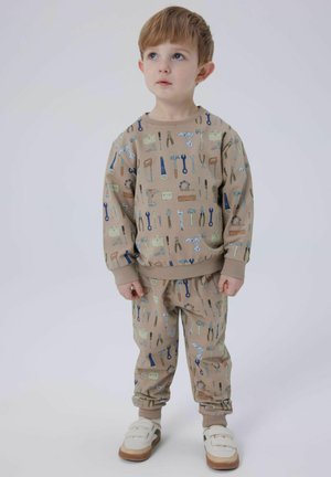 Completo in felpa beige con motivo di attrezzi, realizzato in tessuto morbido. La parte superiore ha un colletto rotondo e polsini, mentre i pantaloni hanno una vita elastica e polsini.