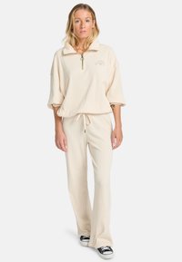 Cremfarbener Lounge-Set in gerippter Textur, bestehend aus einem pullover mit halbem Reißverschluss und Kragen sowie einer lockeren Jogginghose mit Kordelzug.